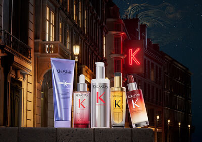 An arrangement of various hair care products featuring the letter "K," displayed in front of a city street at night with a glowing neon sign.