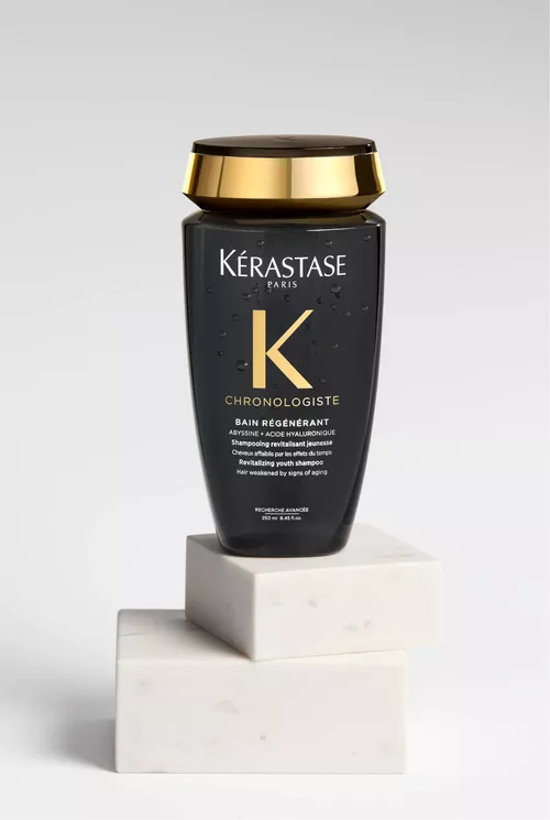 Shampoo Chronologiste nero e oro su un'elegante piattaforma di marmo.