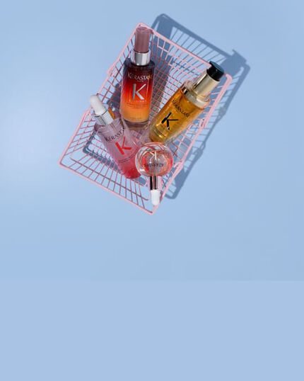 Quattro prodotti per capelli Kerastase in mini-carrelli rosa su sfondo nero: il Siero Notte 8H Nutritive, l'Olio Originale Elixir Ultime, il Siero Anti-caduta Fortificante di Genesis e le Glaze Drops.