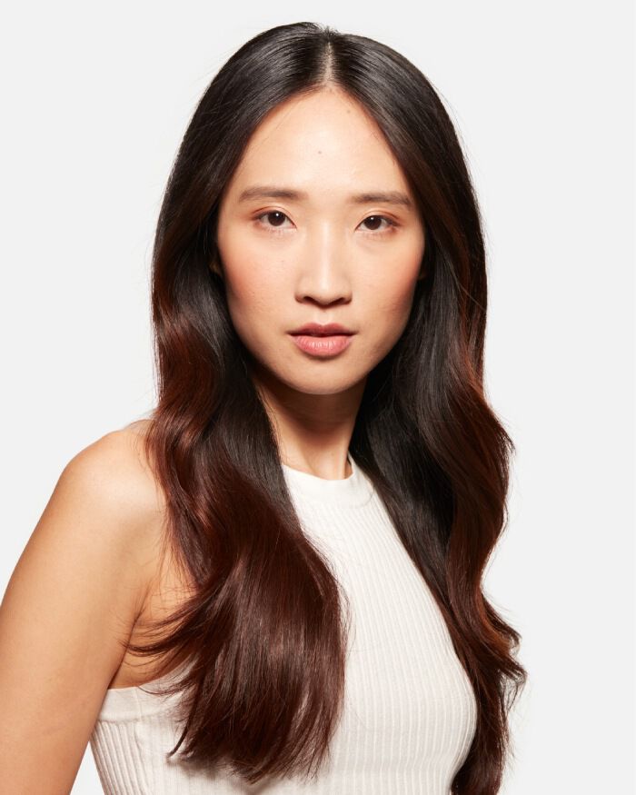 Ritratto ravvicinato di una donna con capelli lunghi e ondulati, che indossa una maglietta bianca. Ha un'espressione intensa e guarda verso l'obiettivo.