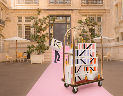A stylish outdoor area featuring pink stairs, modern signage for Kerastase, and shaded seating under umbrellas.