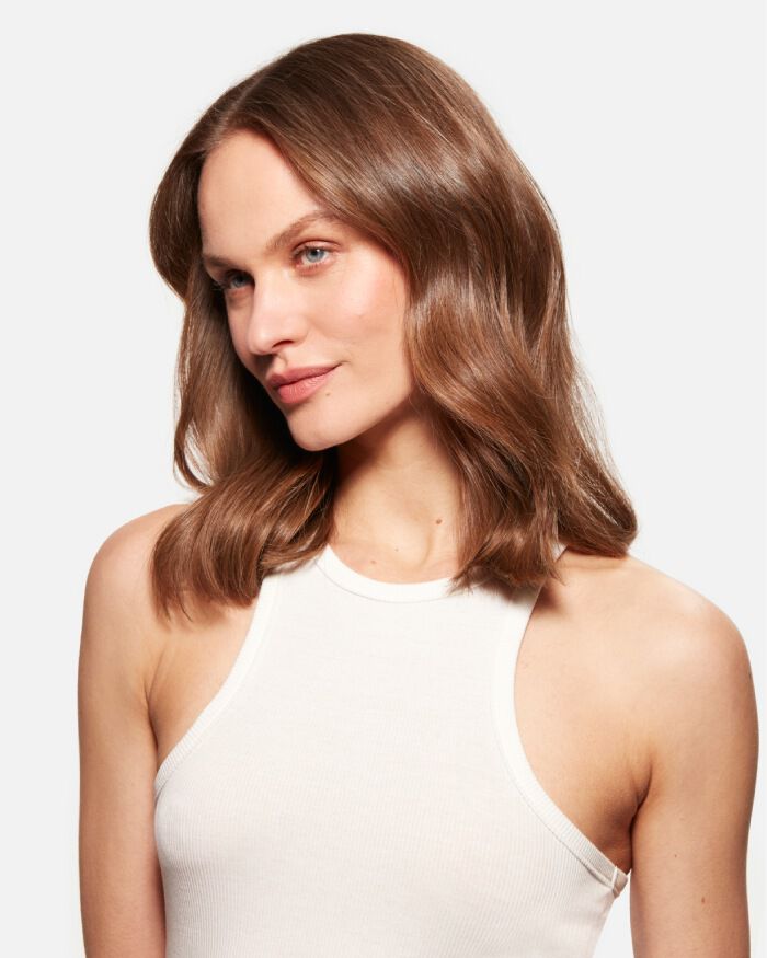 Ritratto di una giovane donna con capelli castani ondulati, che indossa una maglietta bianca senza maniche e sorride leggermente.