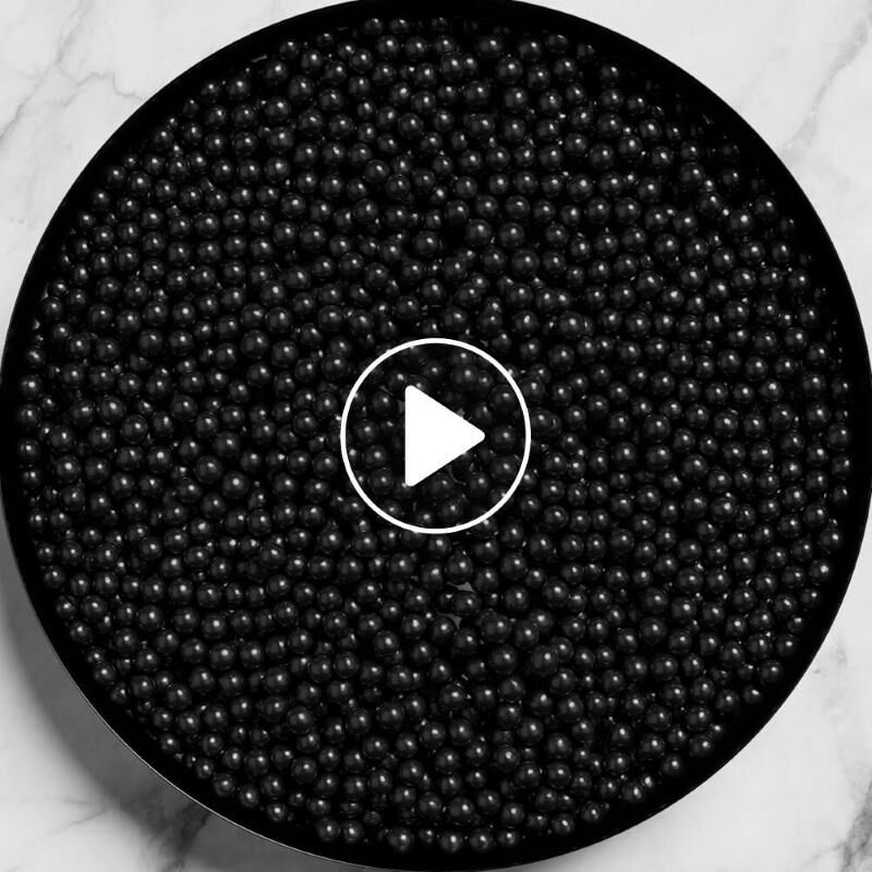 Una vista dall'alto di un contenitore circolare pieno di tante piccole perle nere lucide su una superficie di marmo.