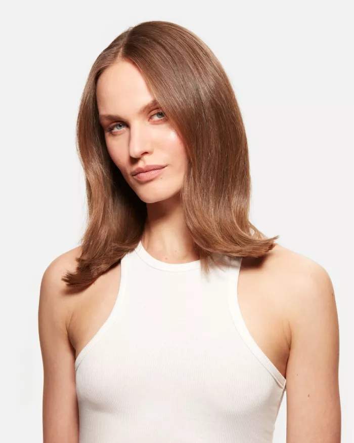 Ritratto di una donna con capelli lunghi e lisci, che indossa un top bianco. Ha uno sguardo sicuro e diretto.
