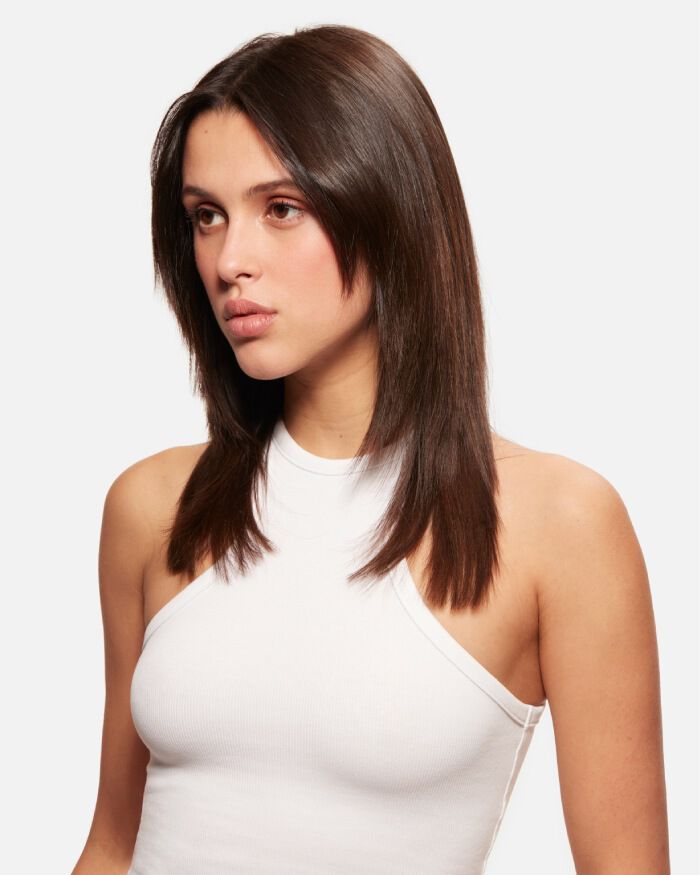 Ritratto di una giovane donna con capelli lunghi e lisci, che indossa una canotta bianca. La sua espressione e serena e guarda verso sinistra.