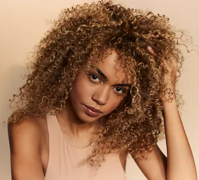 Ritratto di donna con capelli ricci, voluminosi e naturali, a illustrazione di come integrare un prodotto antiumidita nella routine per capelli