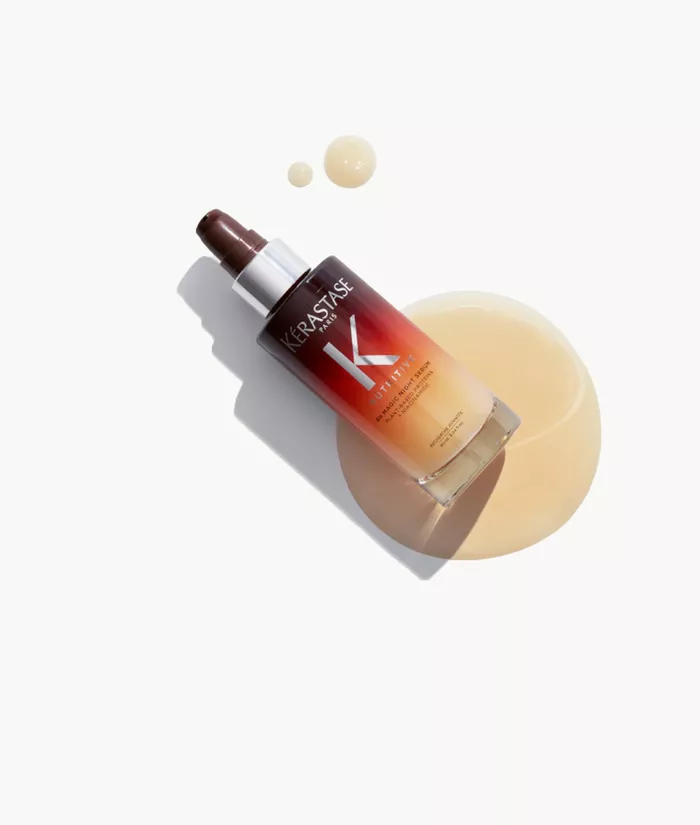 Flacone di siero per capelli Kerastase, con una goccia di prodotto accanto, su sfondo chiaro.