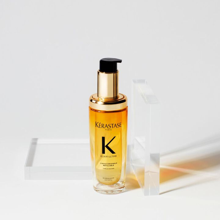 Flacone di siero Kerastase Elixir Ultime con etichetta nera e oro, posizionato su una superficie chiara accanto a una lastra trasparente.