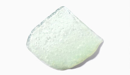 Un frammento di vetro verde chiaro su sfondo bianco.