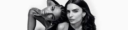 Black and white photograph of two women with contrasting hairstyles and expressions, posing intertwined against a plain background.