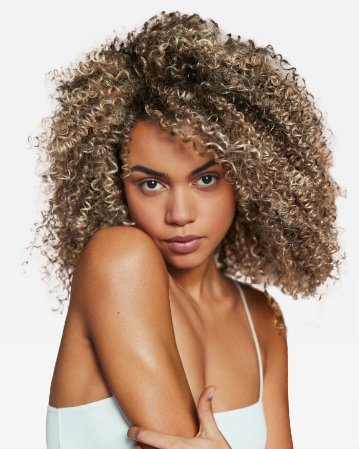 Ritratto di una giovane donna con capelli ricci e biondo scuro, che guarda verso la fotocamera con espressione serena.