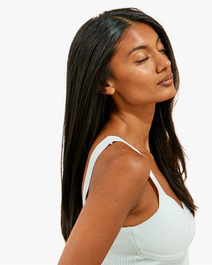 Donna con lunghi capelli lisci che indossa un top chiaro, con lo sguardo rivolto verso l'alto e gli occhi chiusi.