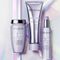 Three Kerastase hair care products are displayed against an iridescent background. The products include a jar, a tube, and a spray bottle, all from the "Blond Absolu" line, featuring a soft purple color scheme.
