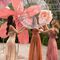Three women in a botanical setting are joyfully interacting with a large, transparent orb surrounded by vibrant flower decorations.