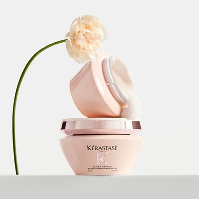 Due barattoli di maschera per capelli Kerastase Gloss Absolu con texture bianca cremosa che fuoriesce e un garofano rosa pallido.