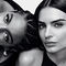 Two models pose together in a black and white photo. One model is leaning back with her head tilted, while the other faces forward, both displaying confident expressions.