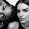 Two models pose together in a black and white photo. One model is leaning back with her head tilted, while the other faces forward, both displaying confident expressions.