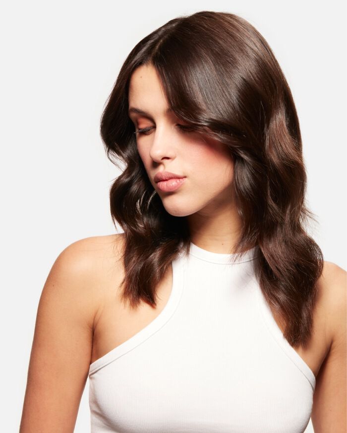 Ritratto di una giovane donna con capelli castani ondulati, che guarda in basso con un'espressione tranquilla, indossando una maglietta senza maniche.