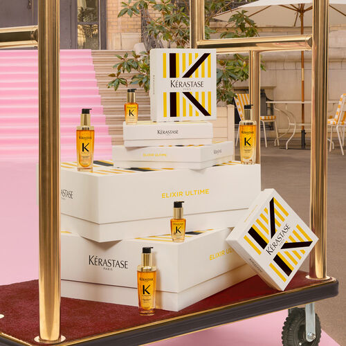 A stylish display of Kerastase hair care products, featuring elegant boxes and bottles arranged in front of a gold-framed mirror, with a backdrop of a modern, bright outdoor setting.