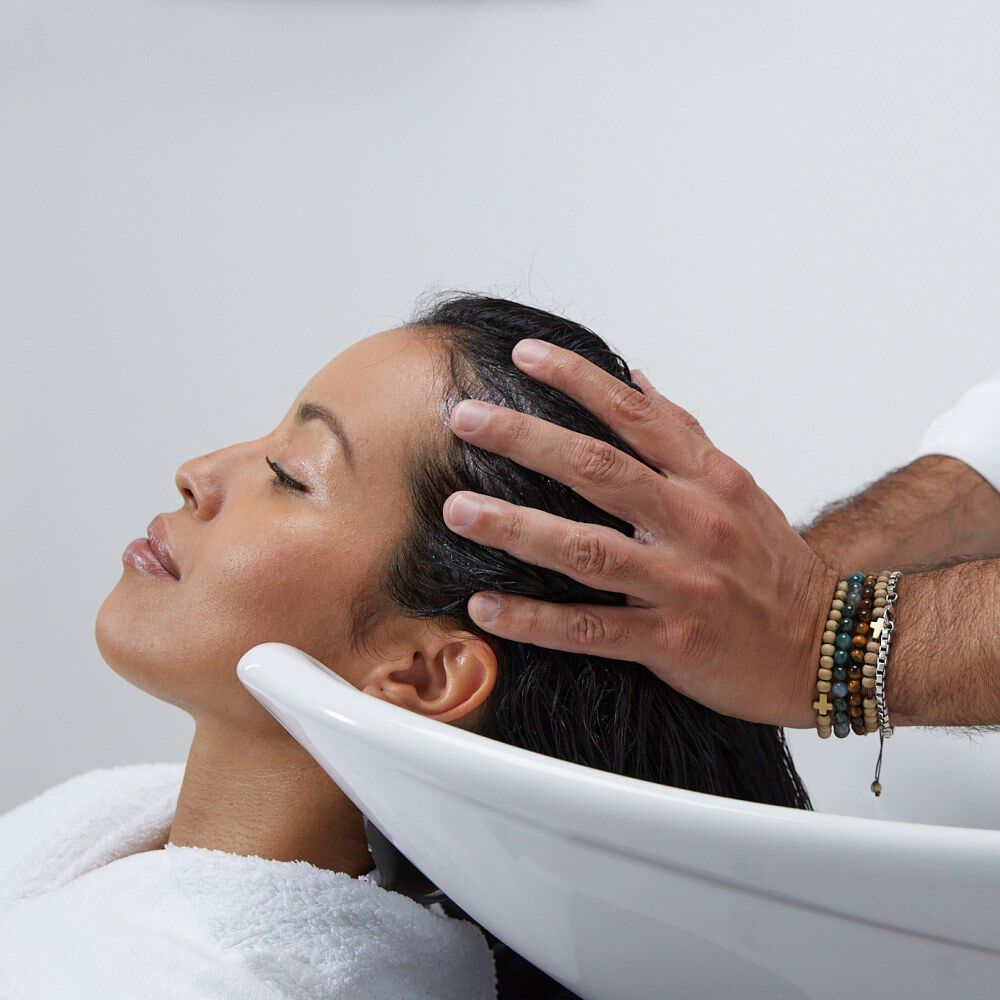 Una donna riceve un massaggio al cuoio capelluto mentre e sdraiata in una postazione per shampoo.