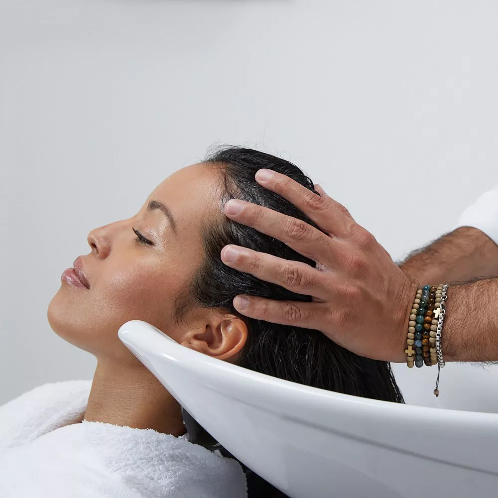 Una donna riceve un massaggio al cuoio capelluto mentre e sdraiata in una postazione per shampoo.