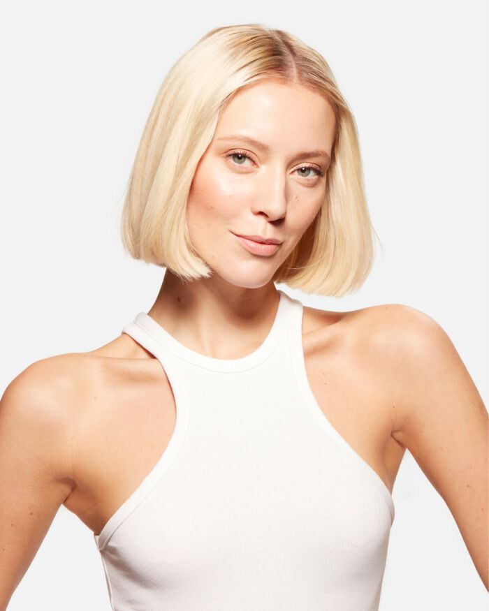 Una giovane donna bionda con un taglio di capelli corto, che indossa una maglietta bianca, guarda verso l'obbiettivo con un'espressione sicura.