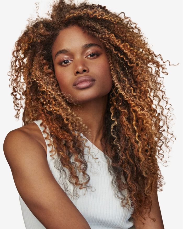 Ritratto di una giovane donna con capelli ricci e voluminosi, che indossa una maglietta bianca, con uno sguardo intenso e naturale.