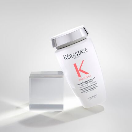 Flacone di shampoo Kerastase, modello "Premiere", inclinato accanto a un cubo trasparente su sfondo chiaro.