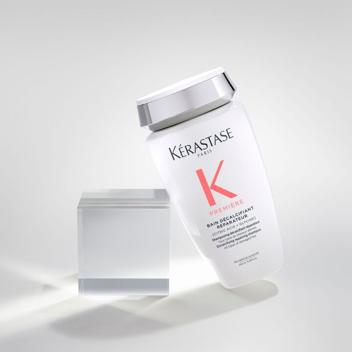 Flacone di shampoo Kerastase, modello "Premiere", inclinato accanto a un cubo trasparente su sfondo chiaro.