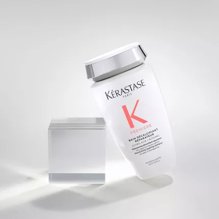 Flacone di shampoo Kerastase, modello "Premiere", inclinato accanto a un cubo trasparente su sfondo chiaro.