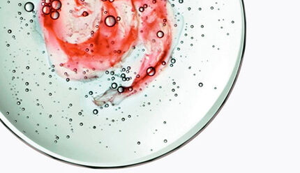 Un piatto trasparente con un vortice di colori rossi e bianchi, circondato da bollicine d'acqua.