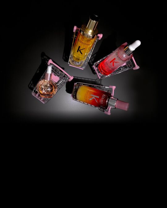 Quattro prodotti per capelli Kerastase in mini-carrelli rosa su sfondo nero: il Siero Notte 8H Nutritive, l'Olio Originale Elixir Ultime, il Siero Anti-caduta Fortificante di Genesis e le Glaze Drops.
