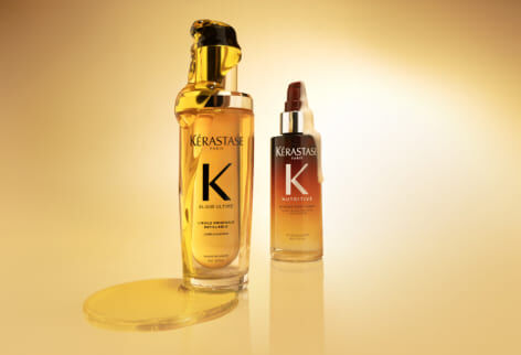 Due prodotti Kerastase, l'Olio Originale Elixir Ultime (flacone dorato) e il Siero Notte 8H Nutritive (flacone con sfumatura arancione), su sfondo giallo dorato.