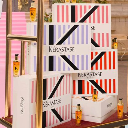 Scatole di prodotti Kerastase Paris in vari colori, con flaconi di shampoo e trattamenti in cima a un carrello elegante.