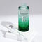A green glass bottle of serum, partially filled with liquid, alongside a pipette, all resting on a white surface with soft shadows.