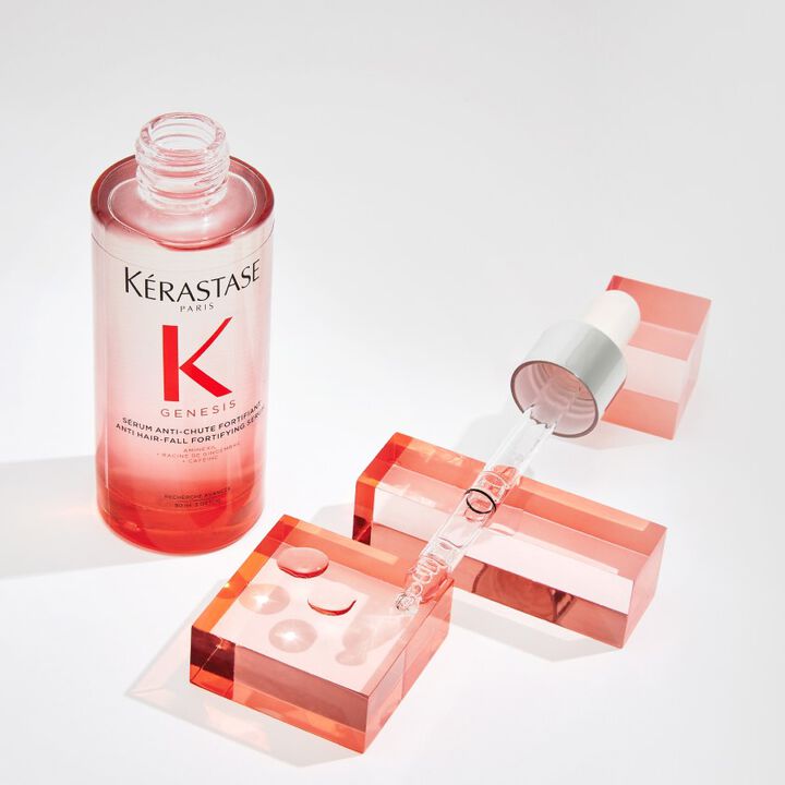 Flacone di siero Kerastase Genesis per la caduta dei capelli, con pipetta e cubi colorati rosa sullo sfondo.
