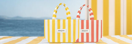 I prodotti Kerastase Huile Elixir 30ml e Serum de Nuit Nutritive sono appoggiati su un telo da spiaggia giallo a righe, vicino alla borsa e alla pochette Kerastase a righe nere.