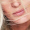 Close-up of a woman's face with blonde hair blowing across her lips, highlighting soft skin and natural beauty.