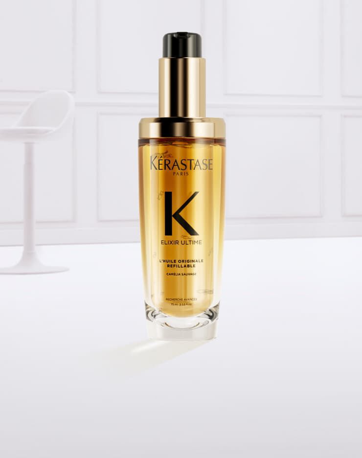 Siero per capelli Kerastase in una bottiglia trasparente con un'etichetta dorata, circondato da spruzzi d'olio dorato.