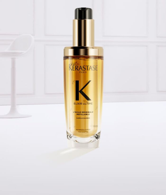 Siero per capelli Kerastase in una bottiglia trasparente con un'etichetta dorata, circondato da spruzzi d'olio dorato.