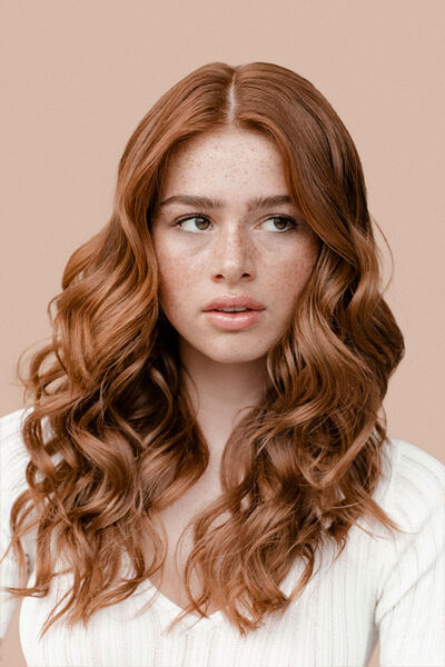 Close-up of a person's eyes and eyebrows with reddish-brown hair against a soft beige background.