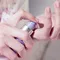 A close-up of a person's hand dispensing a small amount of cream from a lavender-colored pump bottle onto their palm.