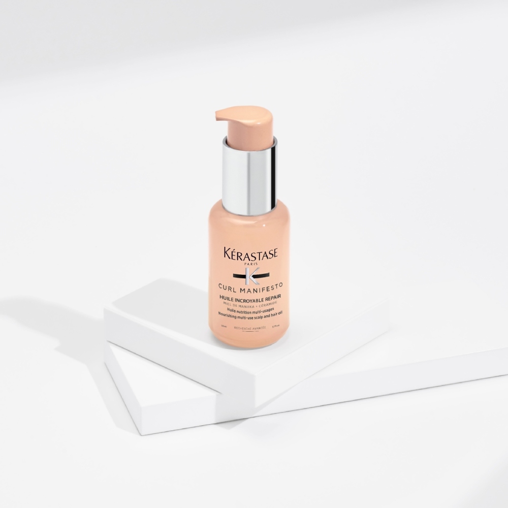 L'olio per capelli Curl Manifesto Huile Sublime Repair è presentato su uno sfondo grigio  con cubi trasparenti. Idrata e modella i ricci mentre agisce contro l'effetto crespo e la rottura.