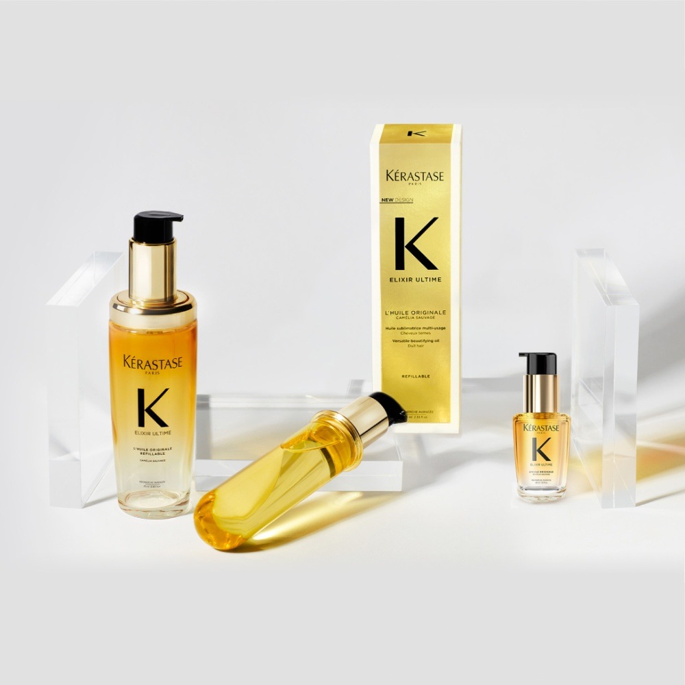 Il nuovo olio per capelli Elixir Ultime, la sua ricarica e il travel size sono presentati su dei cubi trasparenti su sfondo grigio.