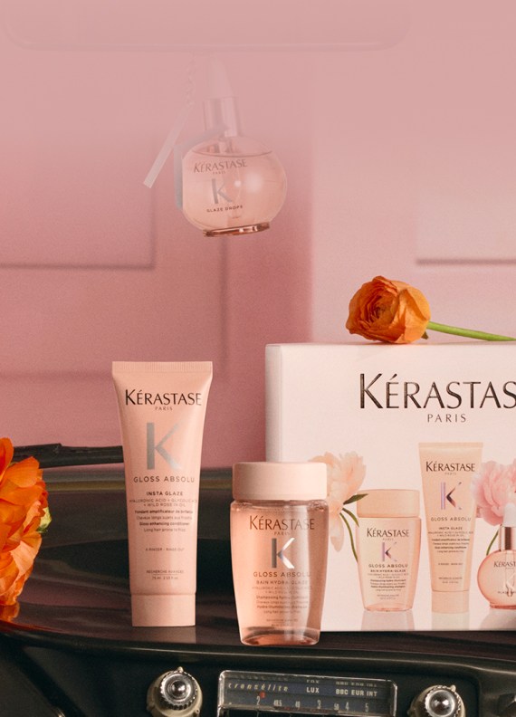 Immagine di prodotti per capelli Kerastase disposti come un regalo, inclusi diversi flaconi dorati, una candela profumata e una pochette bianca in spugna, il tutto presentato in una confezione festiva bianca e dorata su uno sfondo bianco e luminoso. L'insieme evoca lusso ed eleganza.