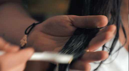 Una mano tiene dei capelli lunghi mentre un'altra mano applica un prodotto con un pennello.