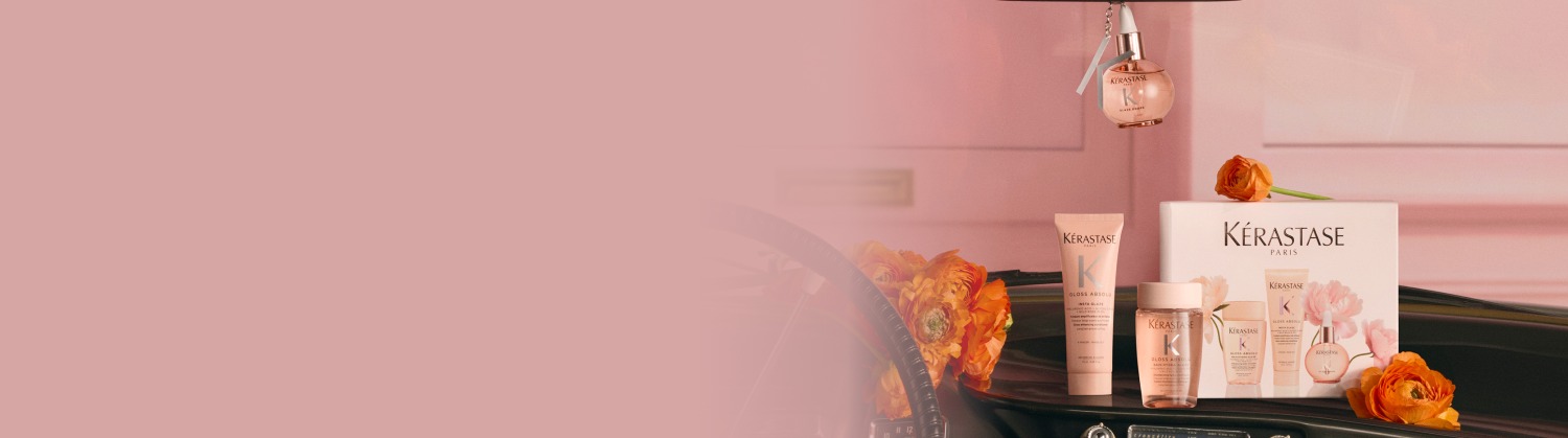 Immagine di prodotti per capelli Kerastase disposti come un regalo, inclusi diversi flaconi dorati, una candela profumata e una pochette bianca in spugna, il tutto presentato in una confezione festiva bianca e dorata su uno sfondo bianco e luminoso. L'insieme evoca lusso ed eleganza.​