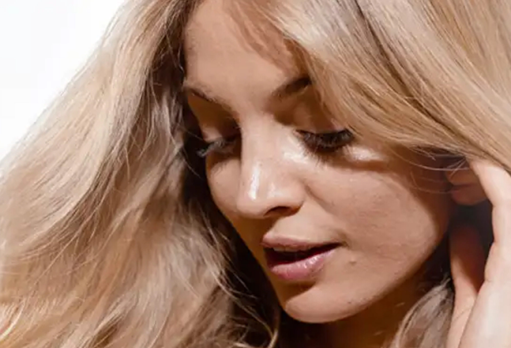 Close-up di una giovane donna con lunghi capelli biondi, mentre guarda verso il basso con espressione delicata.