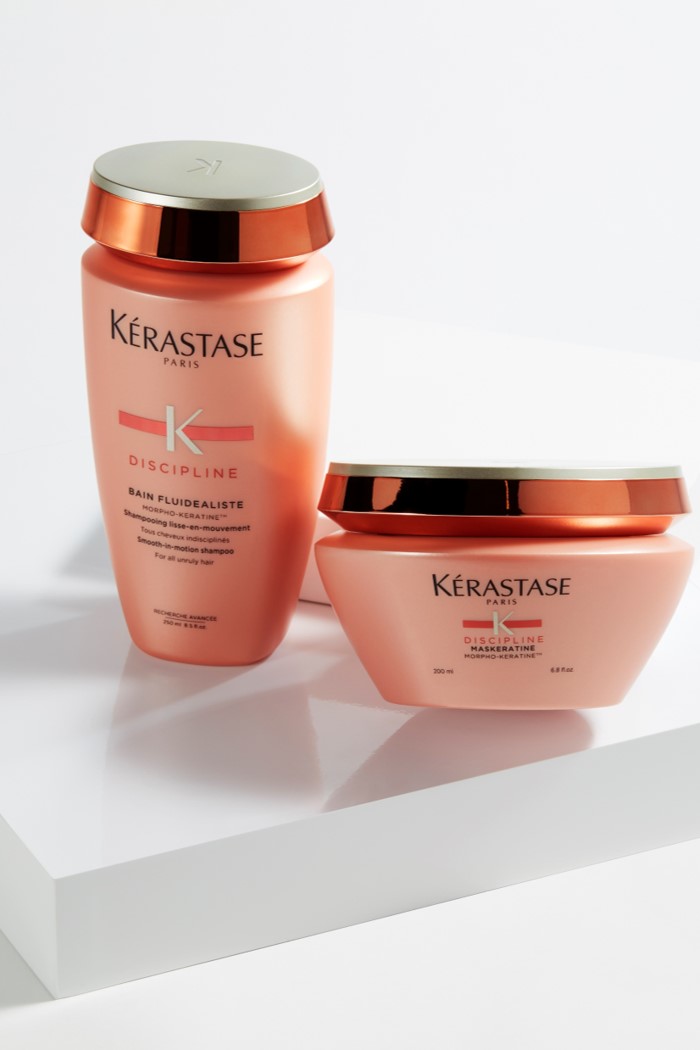 Due flaconi di prodotti per capelli Kérastase Discipline, uno shampoo e un trattamento, su un supporto bianco.