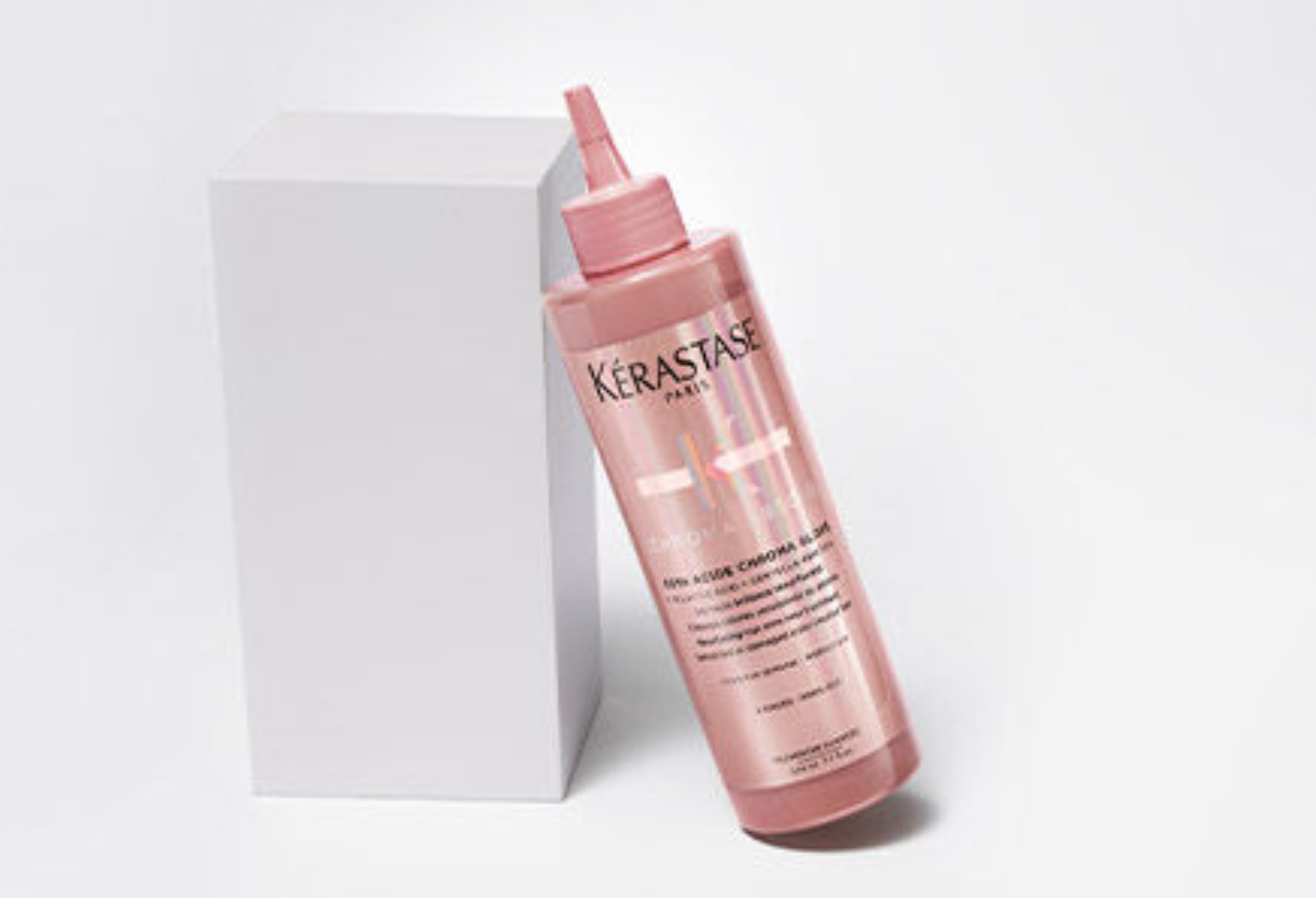 Flacone di trattamento Kérastase in rosa, con applicatore, accanto a un packaging bianco elegante.